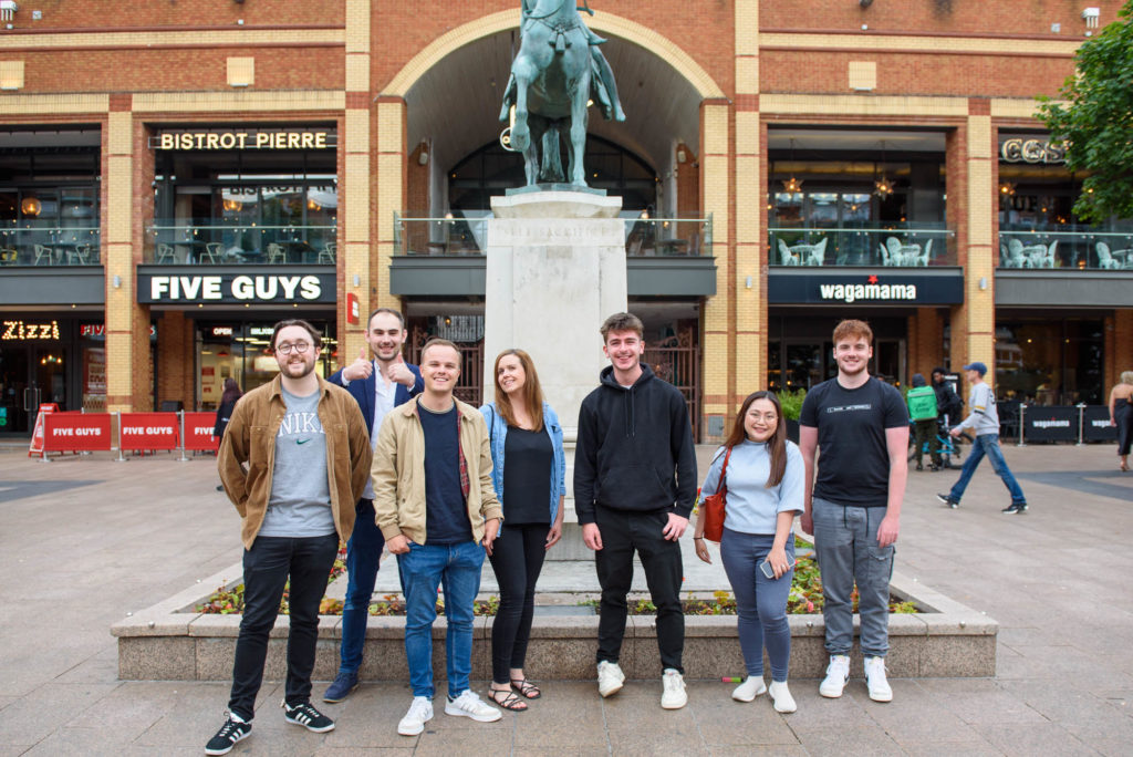  A group of young people poses together in front of a large statue, smiling and enjoying their time outdoors.