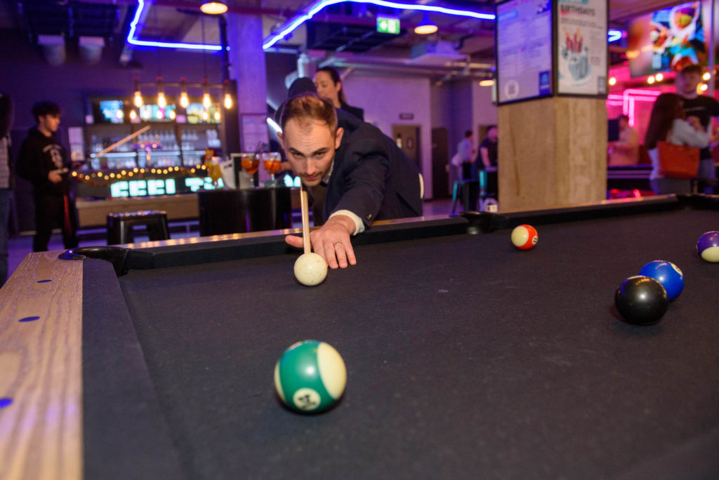 A man leans over a pool table, focusing on the colourful balls arranged on the green felt surface.